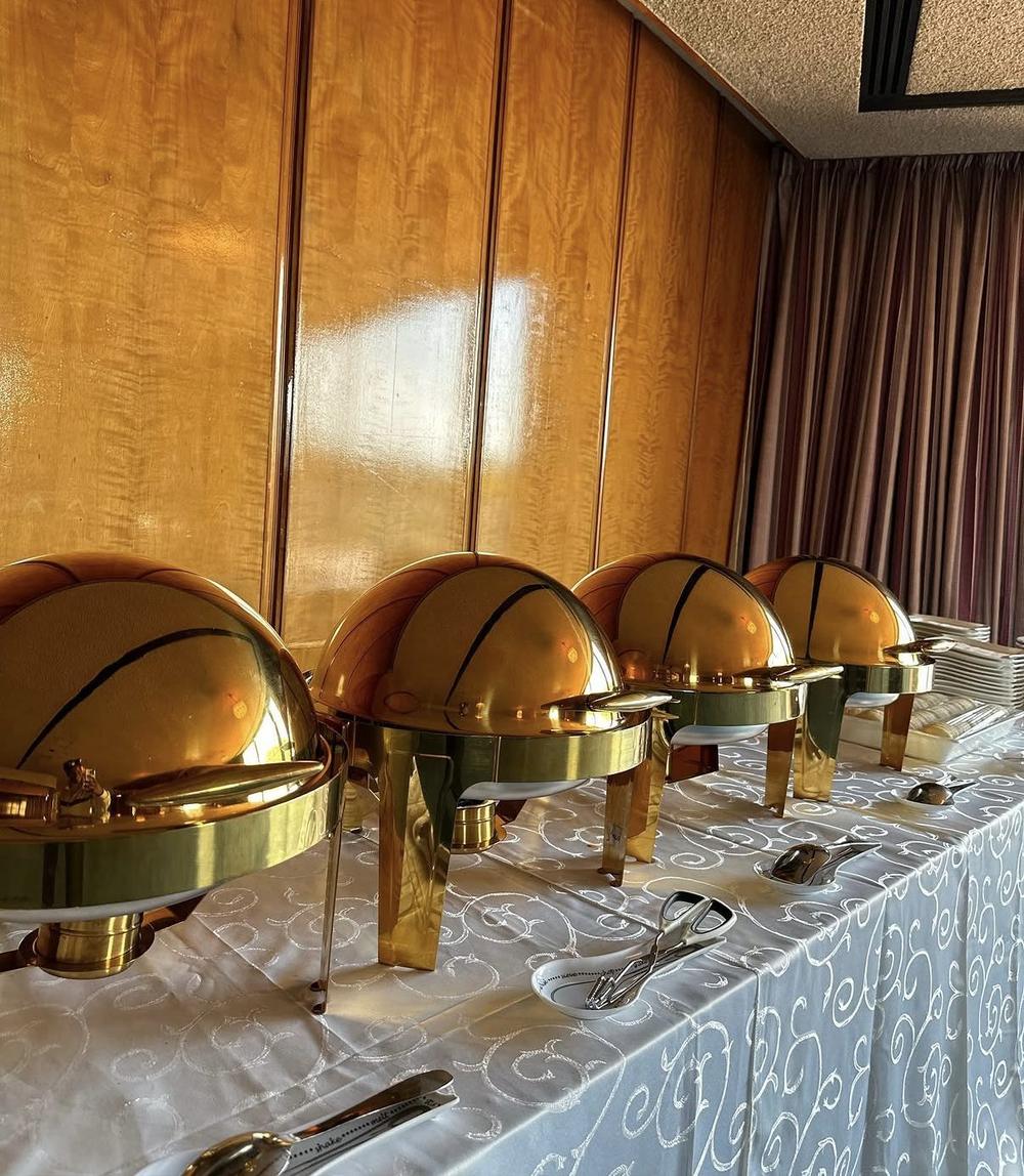 Row of polished gold chafing dishes on a white-linen buffet table